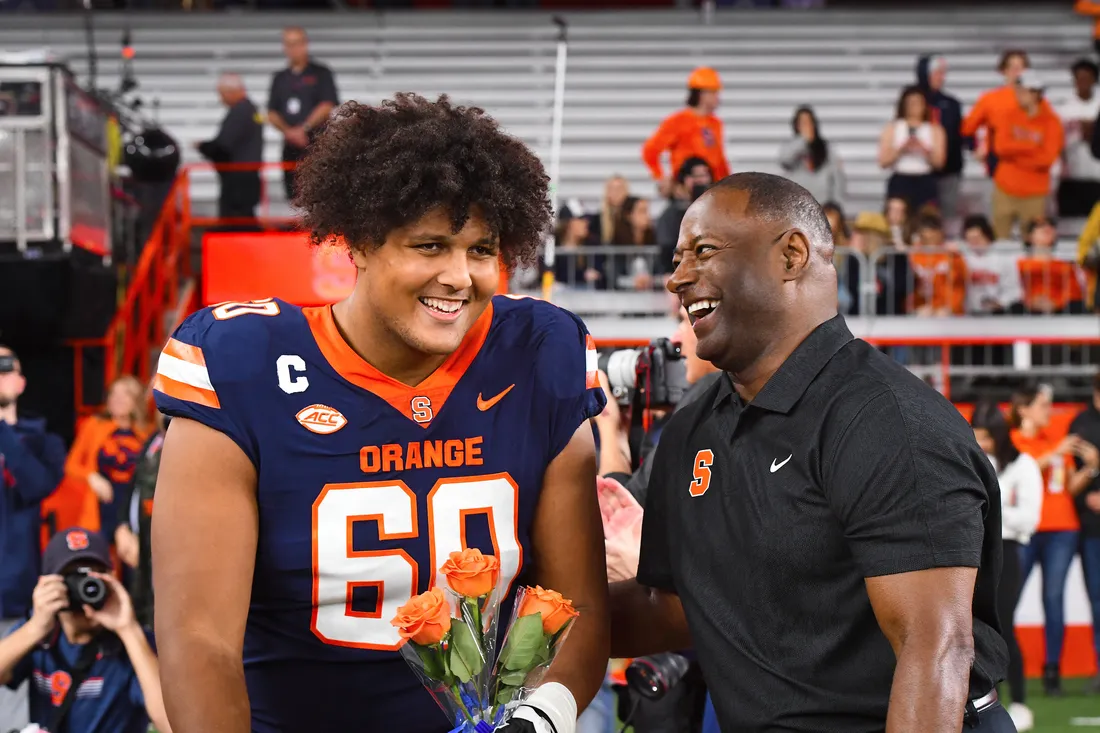 Portrait of Bergeron holding orange roses next to Dino Babers, both laughing.