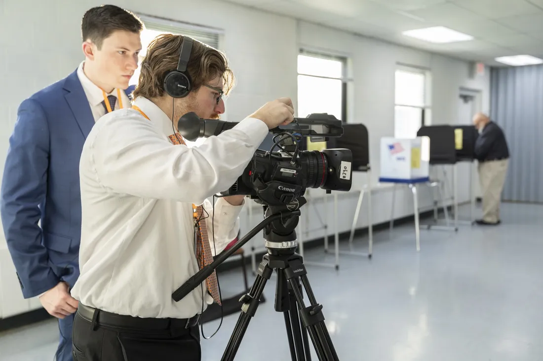 Two people standing behind a video camera.