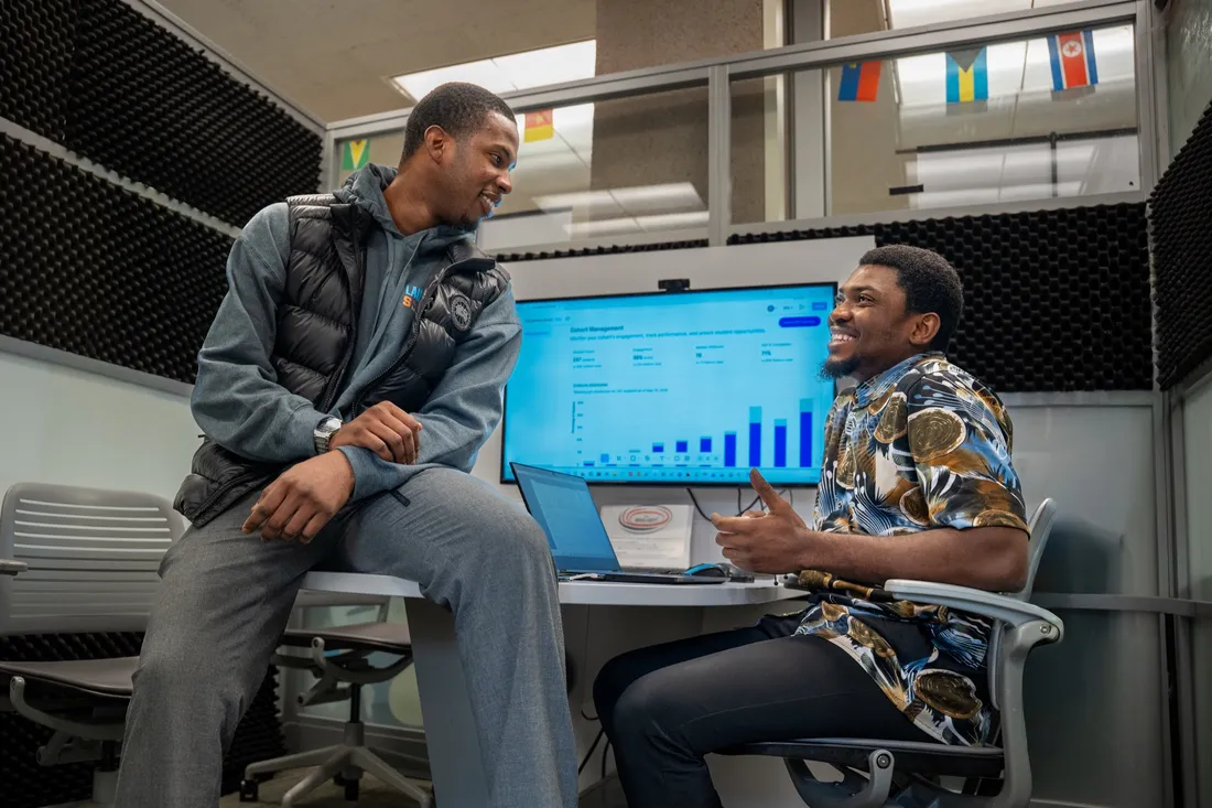 Two students sitting at a desk and speaking.