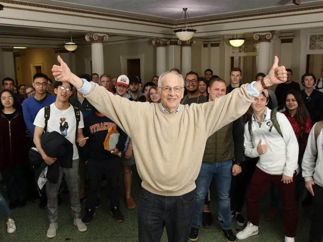 Professor of policy studies Bill Coplin holding up two thumbs up surrounded by his students.