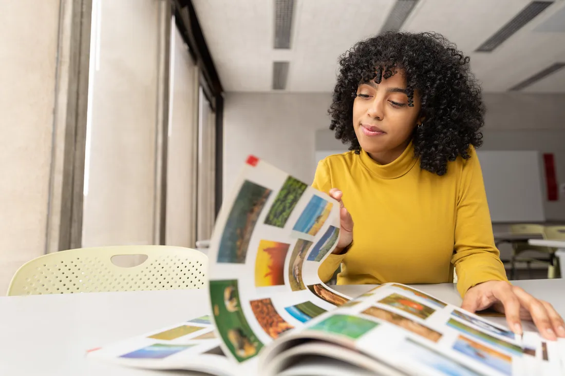 Woman in yellow shirt looks through a magazine.