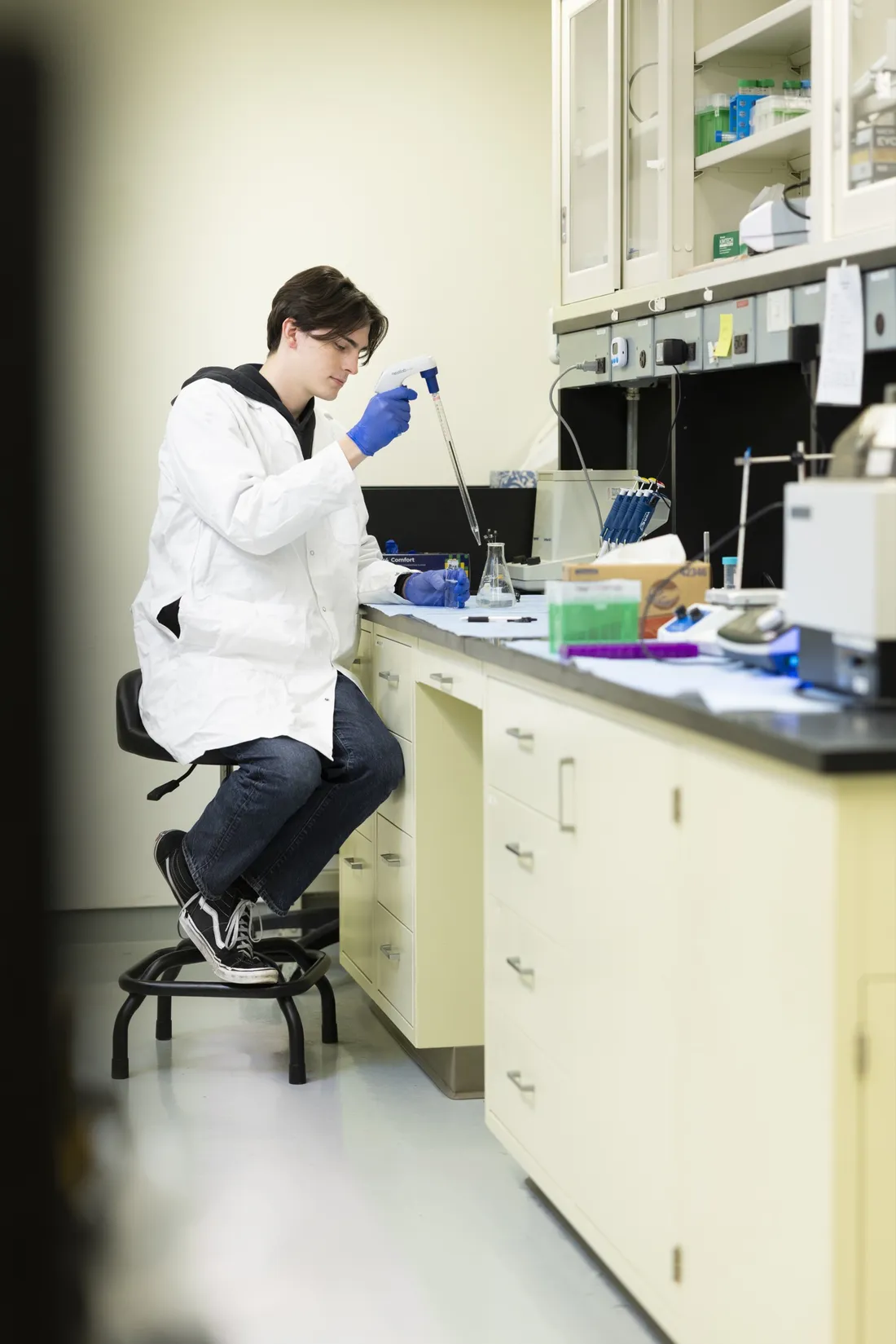 Person sitting at a lab desk using a pipette.