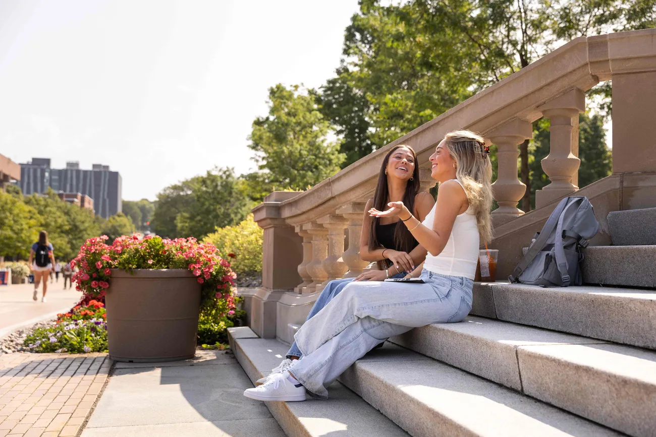 Two students sitting on stairs talking outside.