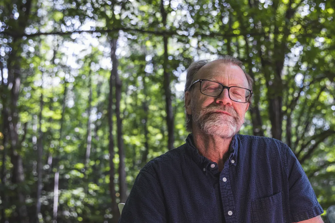 George is smiling with his eyes closed, surrounded by trees.