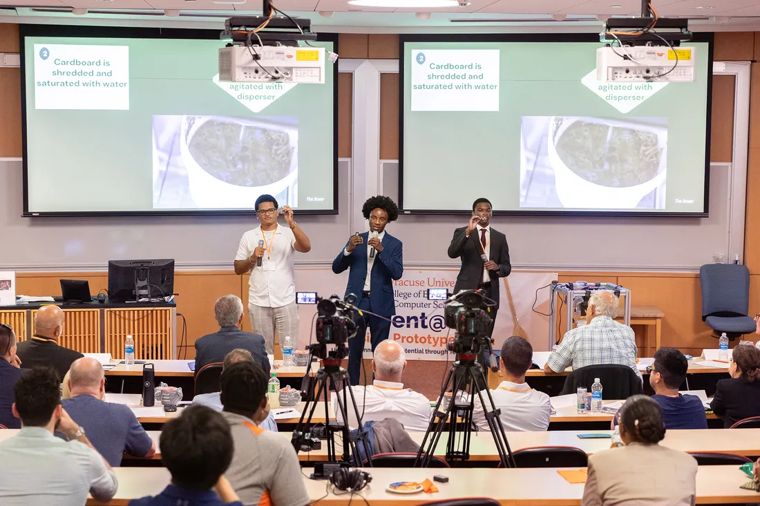 Three students give presentation in lecture hall.