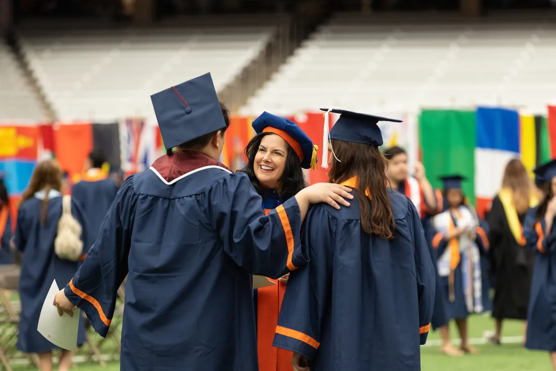 Students sit on steps of building in commencement regalia celebrating graduation.