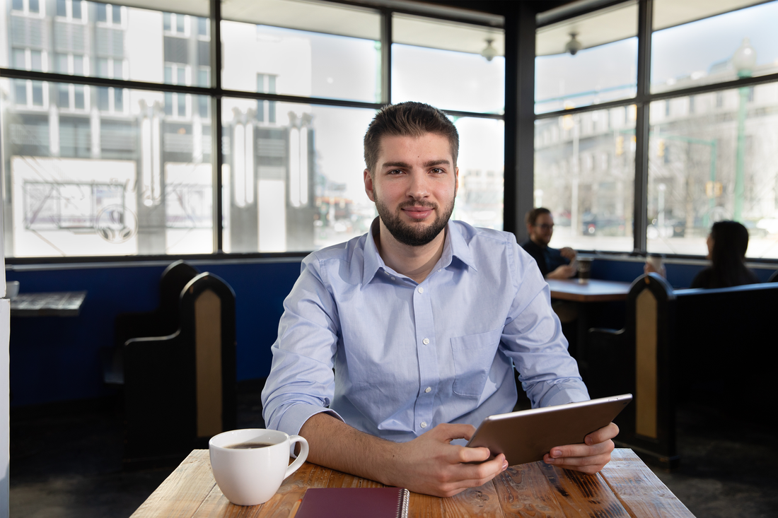 Portrait of Edward Furcinito sitting at a table with a tablet and a cup of coffee.