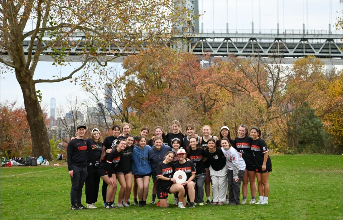 Group of students standing and smiling outside in front of the Manhattan Bridge.