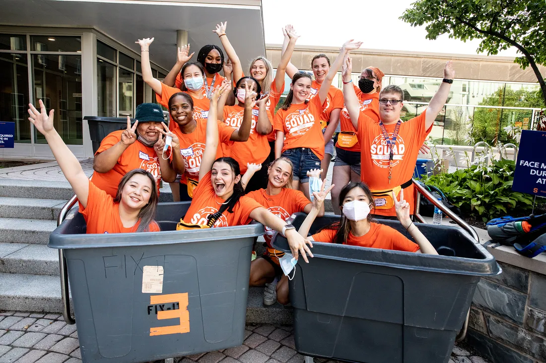 Large group of students make a celebratory pose in large moving bins.