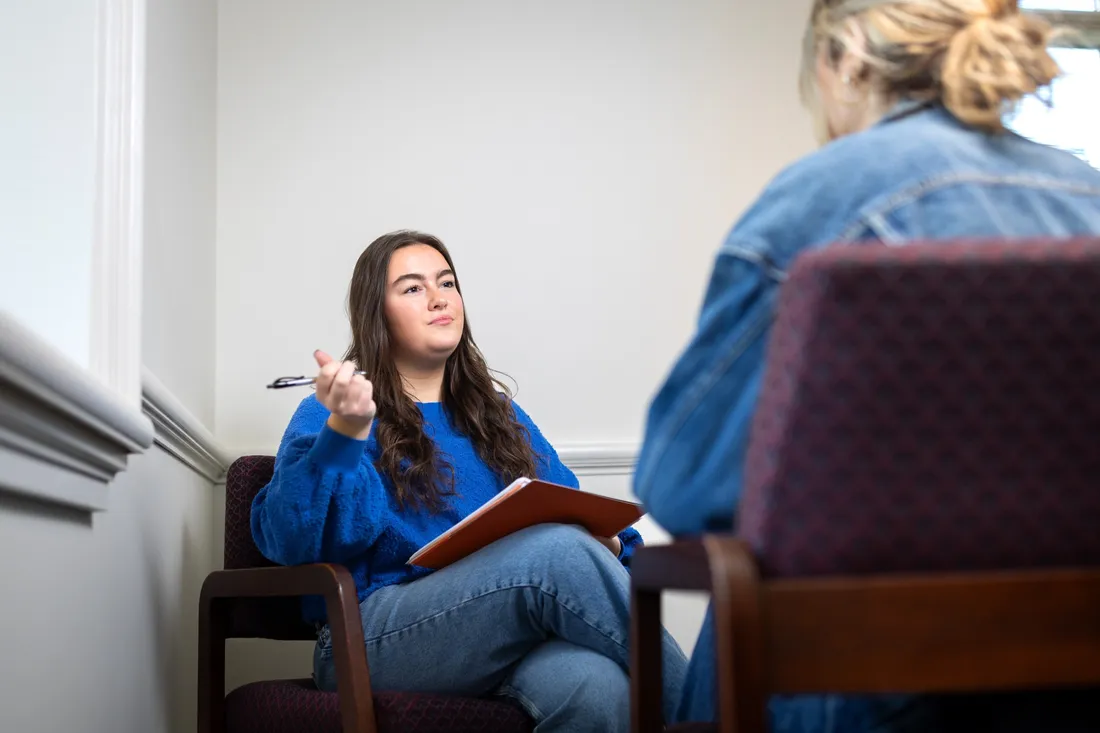 Student Katherine Waters speaking with another student while holding a notebook and pen.