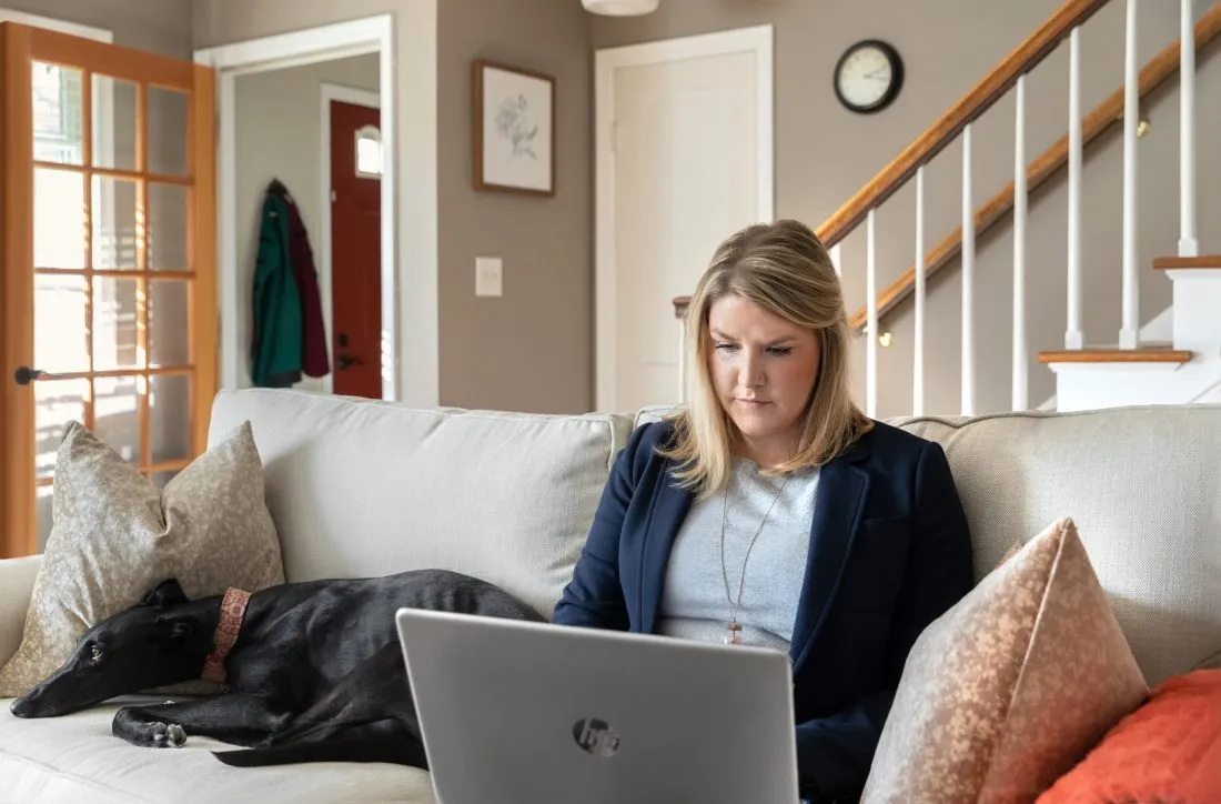 Student learning online from couch, with dog laying beside them.