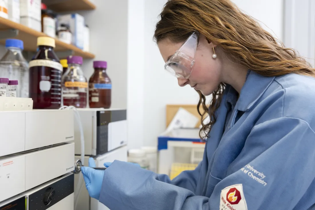 Person wearing lab coat and protective glasses using science equipment.