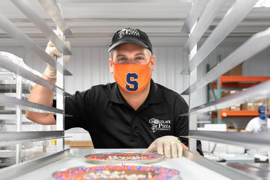 Portrait of Ryan Novak adding a chocolate pizza to a rack.