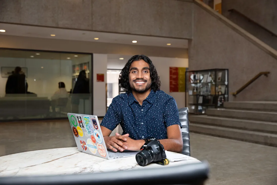 Gaurav Shetty sitting at a table with his laptop open and a camera next to him.