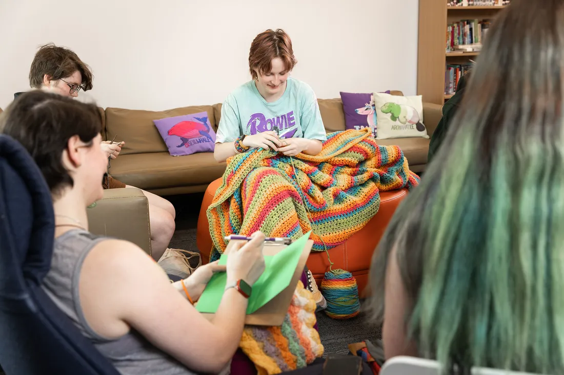 Group of friends sits together on couches knitting.