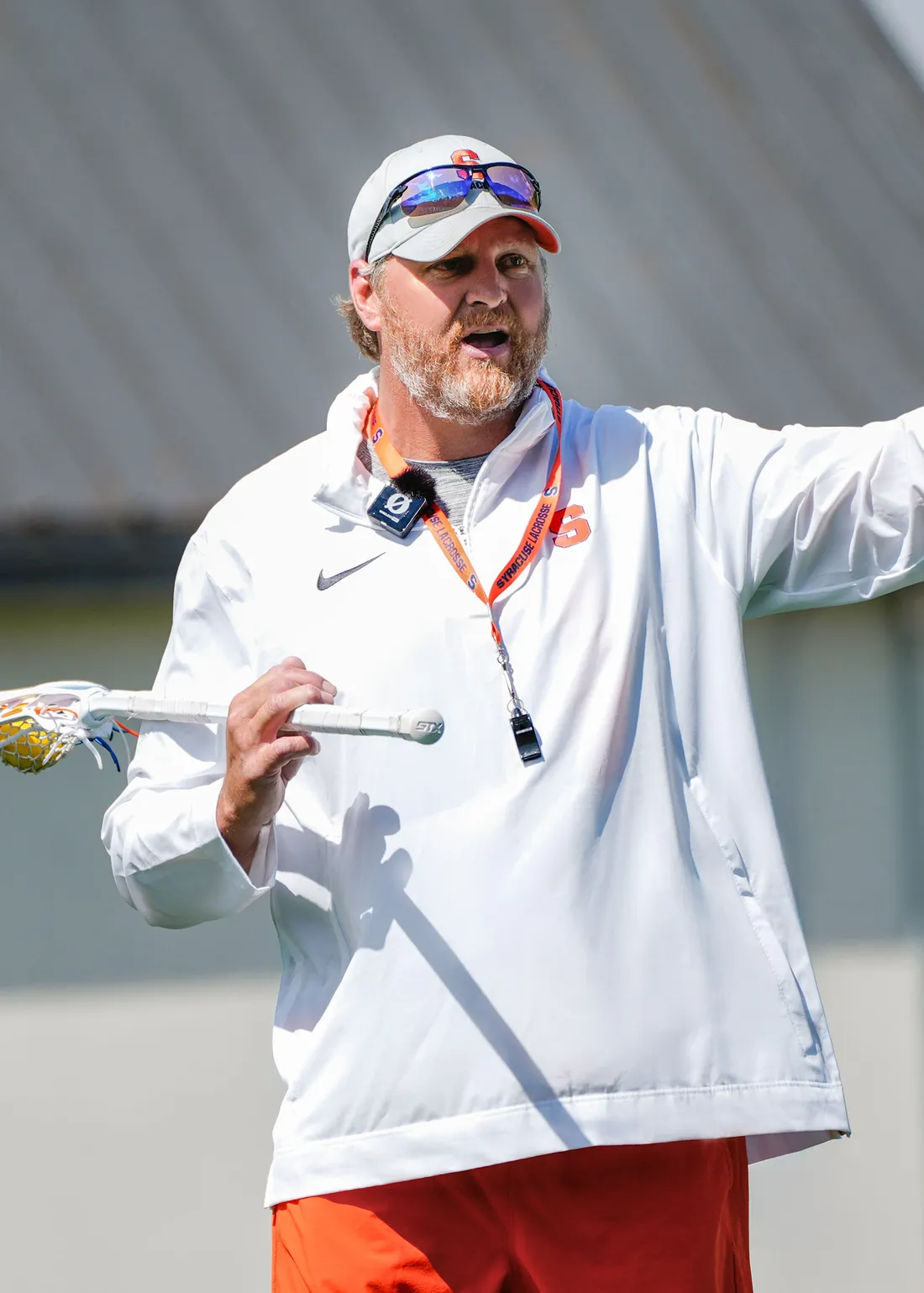 Regy Thorpe on the field of the Dome holding a lacrosse stick and pointing at something.