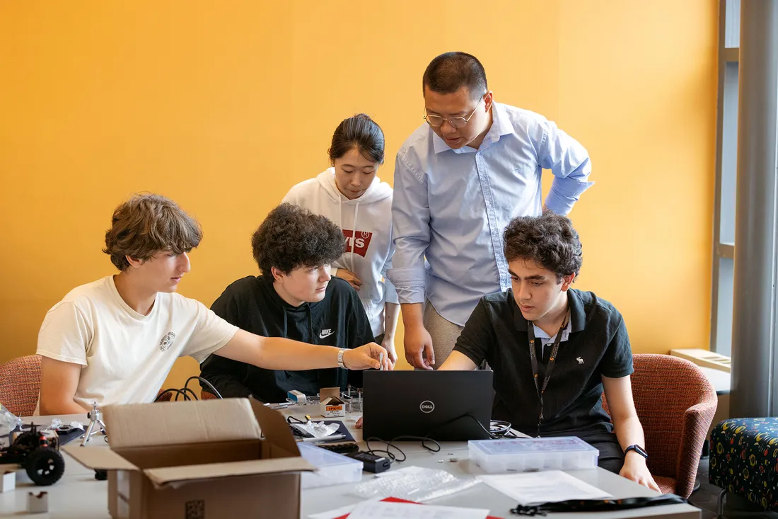 TAs and students look at a laptop.