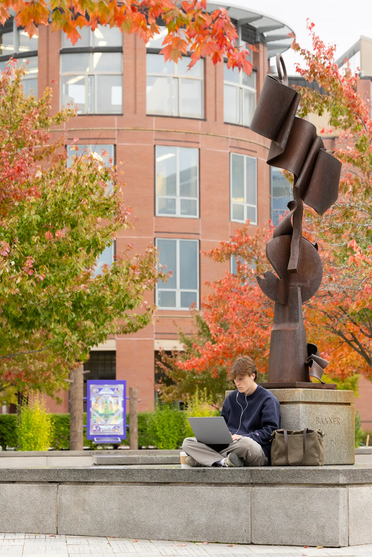 A student sitting on his computer in front of a sculpture on campus.