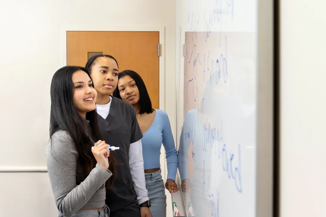 Three female students writing at a white board.