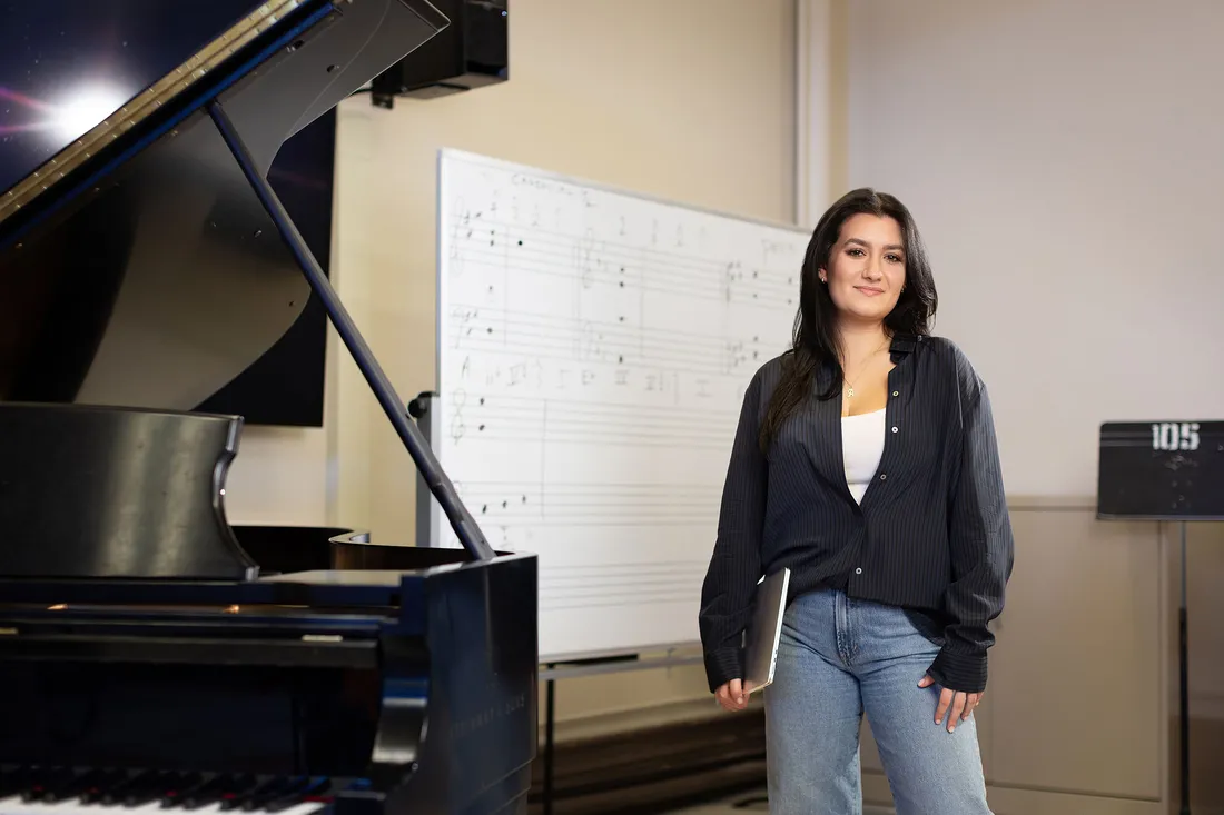 Student smiling in front of a piano and a white board