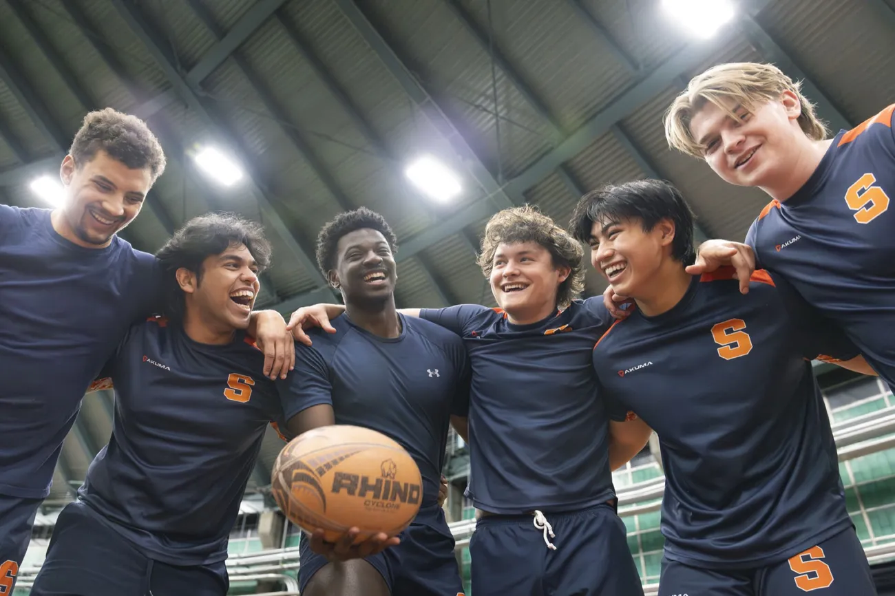 Members of the men's club rugby team standing together with their arms around one another.
