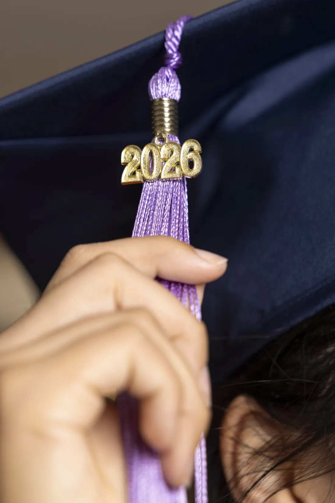 Student grabbing a lavender tassel on their graduation cap with the year 2026 on it.