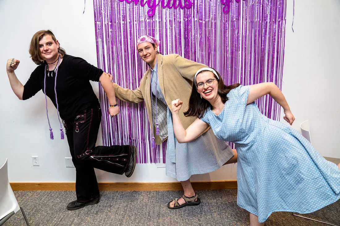 Three students pose together in silly poses in front of lavender tassel backdrop.