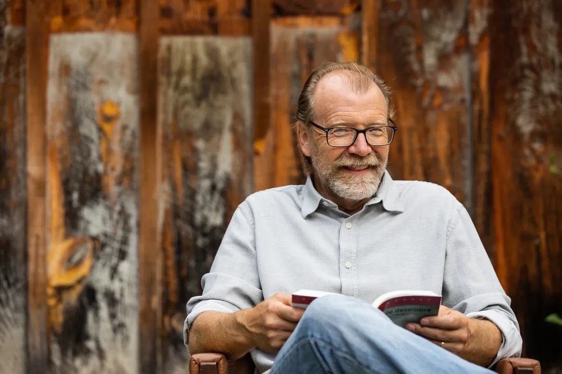 George Saunders sitting and smiling with a book in his hands.