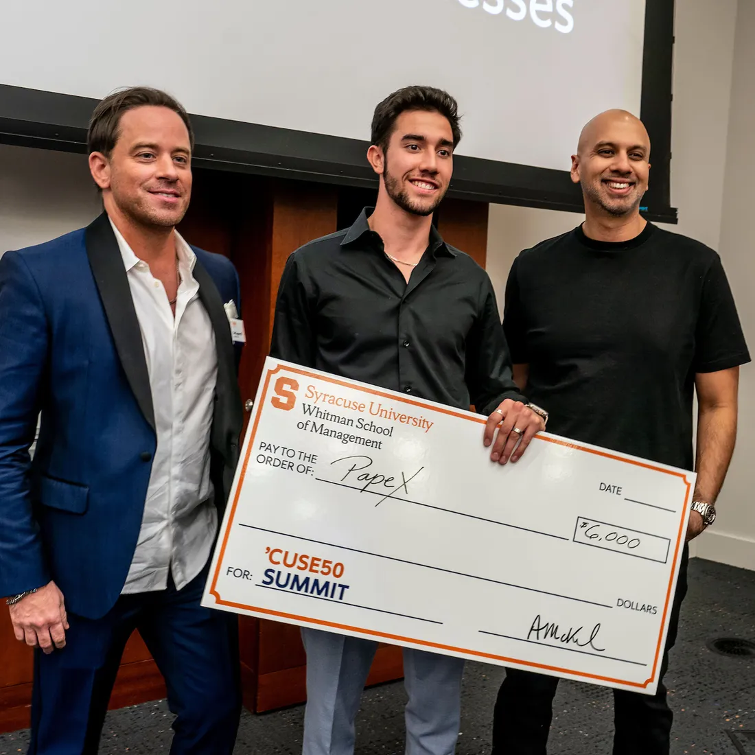 Two alumni standing with a student holding a check.