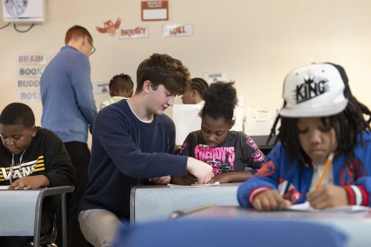 Will Baker '27 sitting next to a student at STEAM at Dr. King Elementary School helping her with her schoolwork.