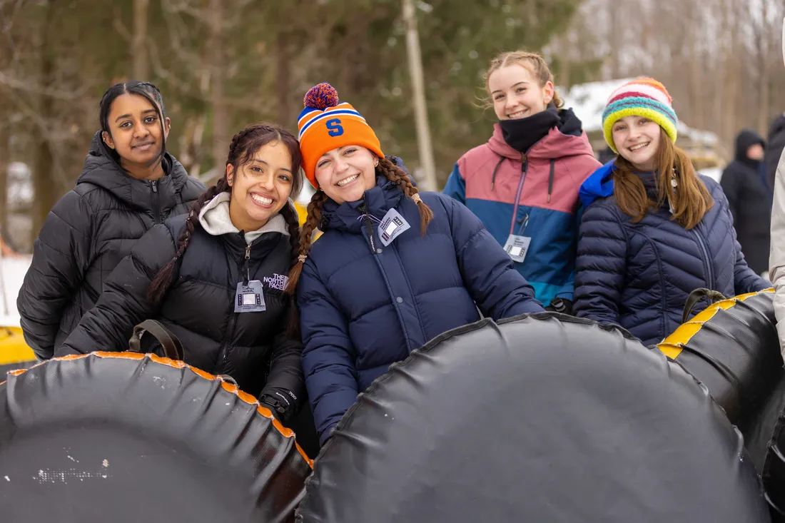 A group of students in winter gear holding snow tubes outside.