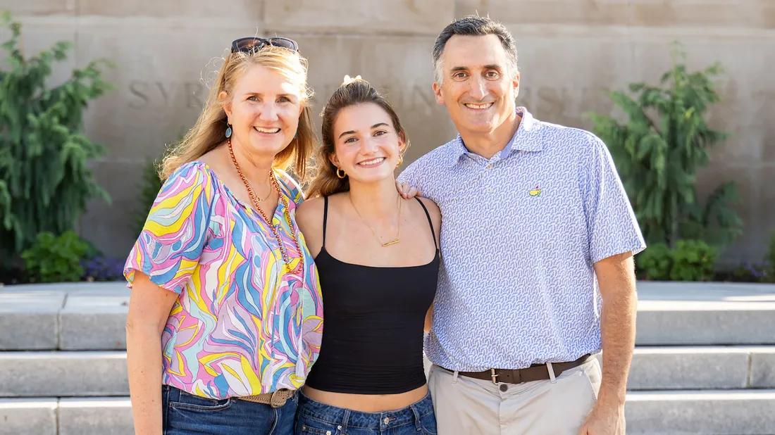 A family of three standing together and posing for a picture on Syracuse University's campus.