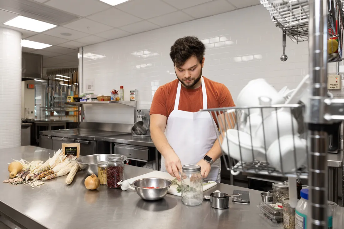 Portrait of Tyo in a test kitchen with ingredients and cooking supplies on the table.