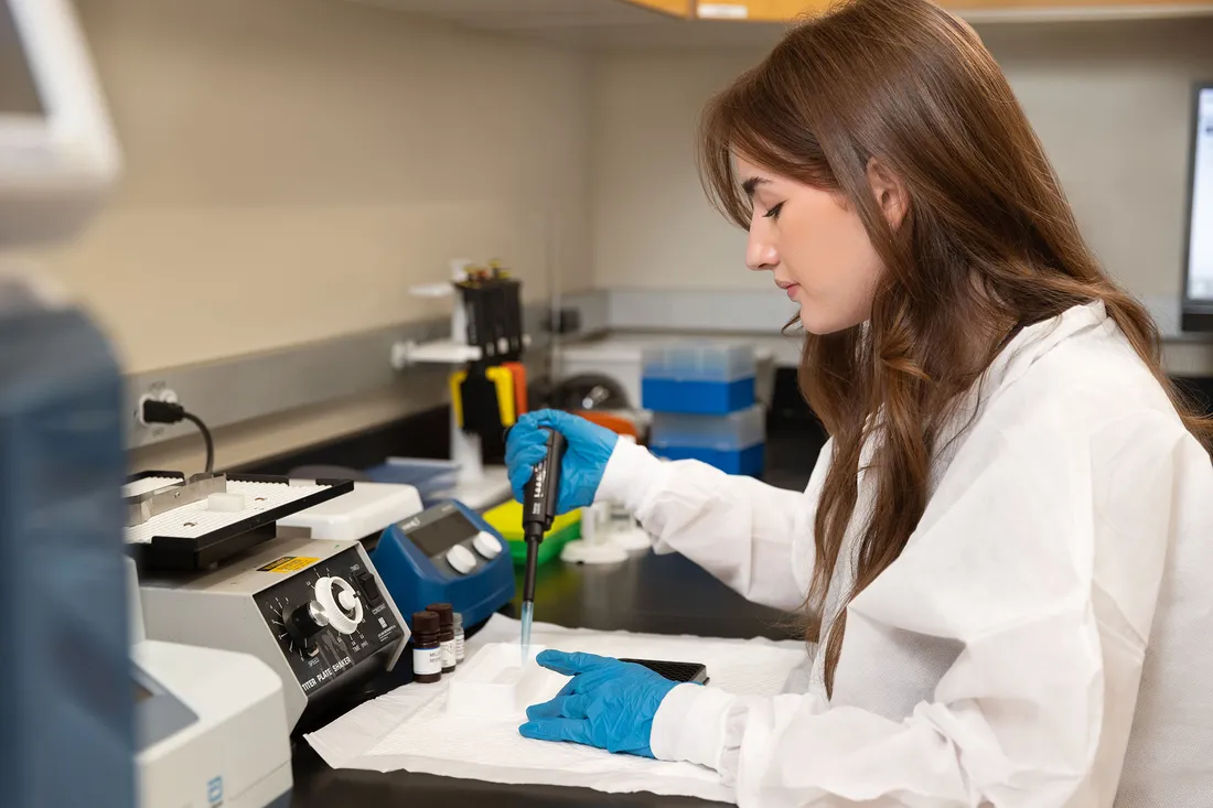 A student with blue gloves is working in a lab