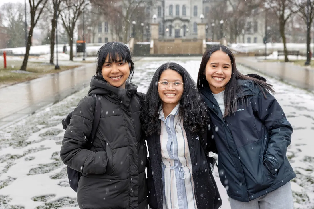 Three students stand outside and smile together.