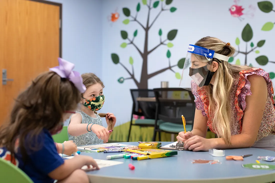 Graduate student and two children color inside a clinic classroom.