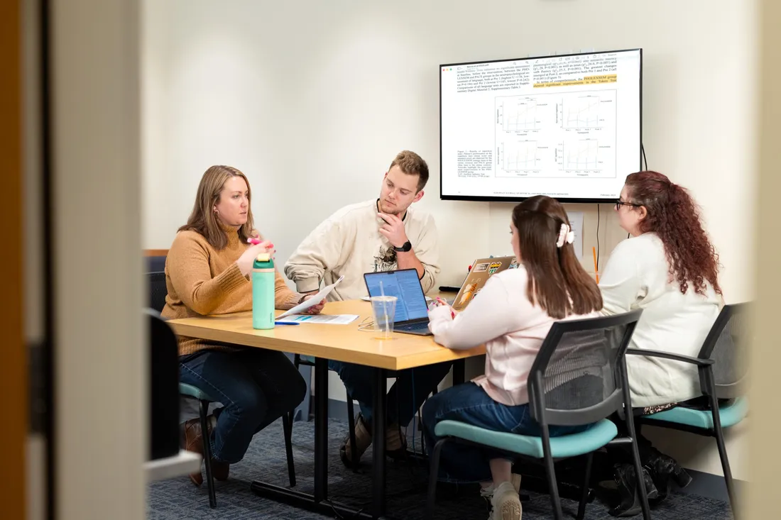 Doctor Ellyn Riley and her team of students and faculty sitting at a table and talking.