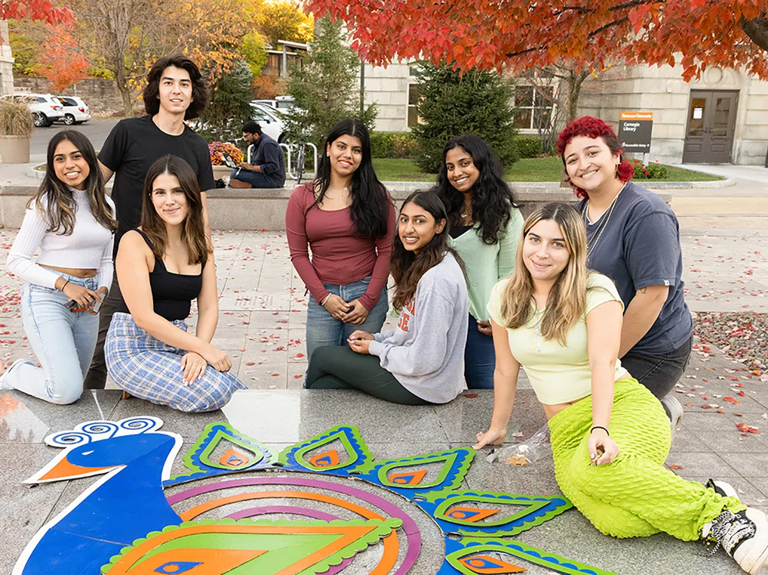 People sitting next to artwork of a peacock.