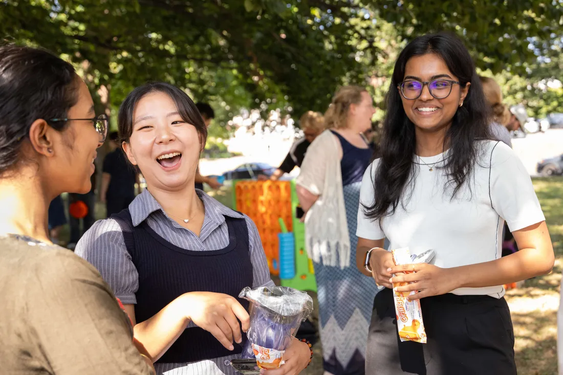 Three international students at an outdoor event, standing and smiling.