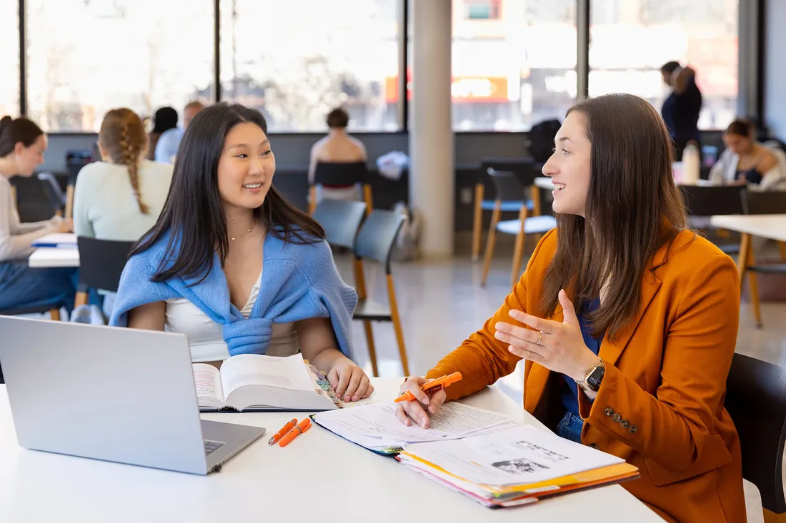 Students sitting and studying at a table while having a conversation.