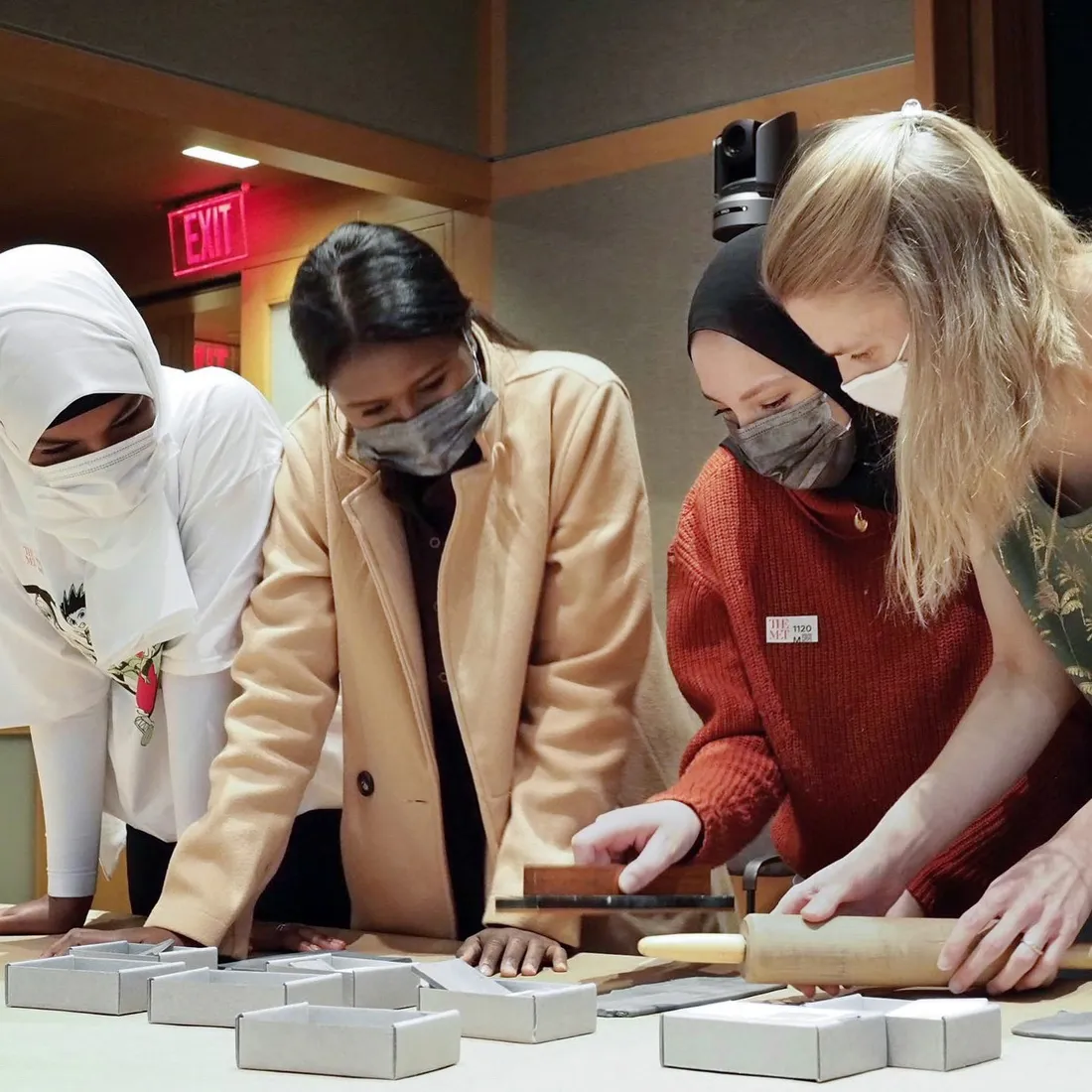 Four women leaning over a table in a museum, looking at objects on it.