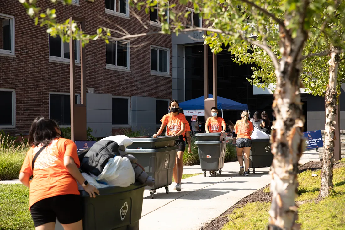 Students outdoors pushing carts filled with belongings on move-in day