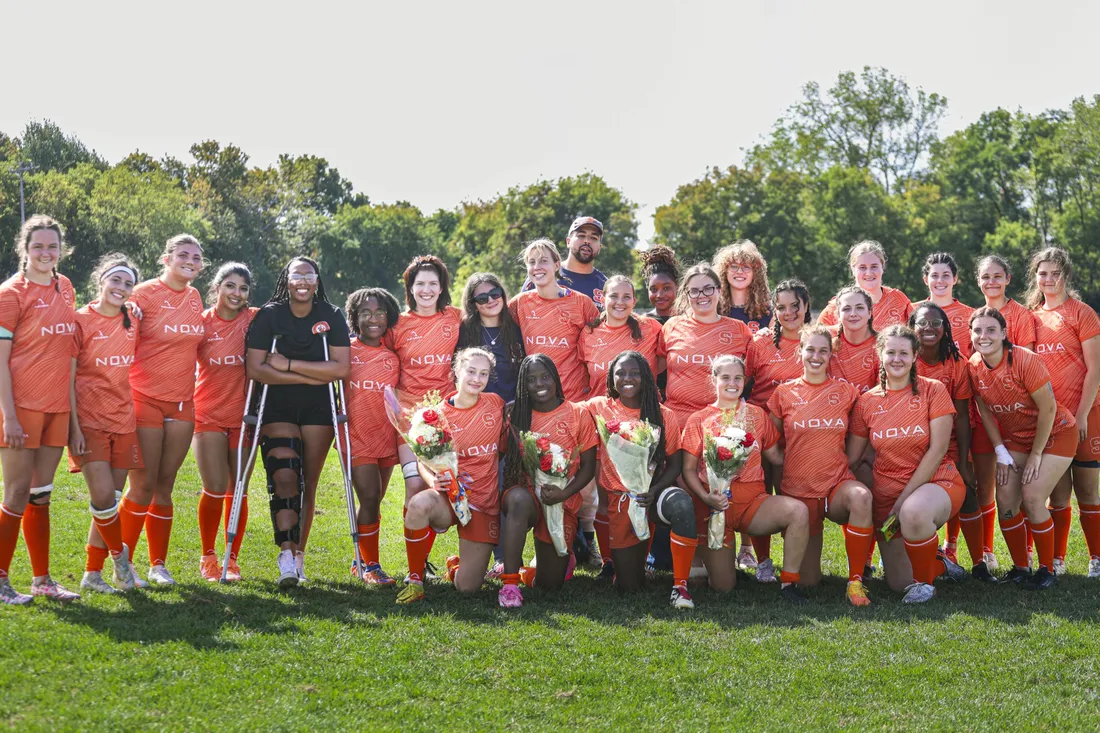 Group photo of the women's club rugby team, accompanied by their coach.