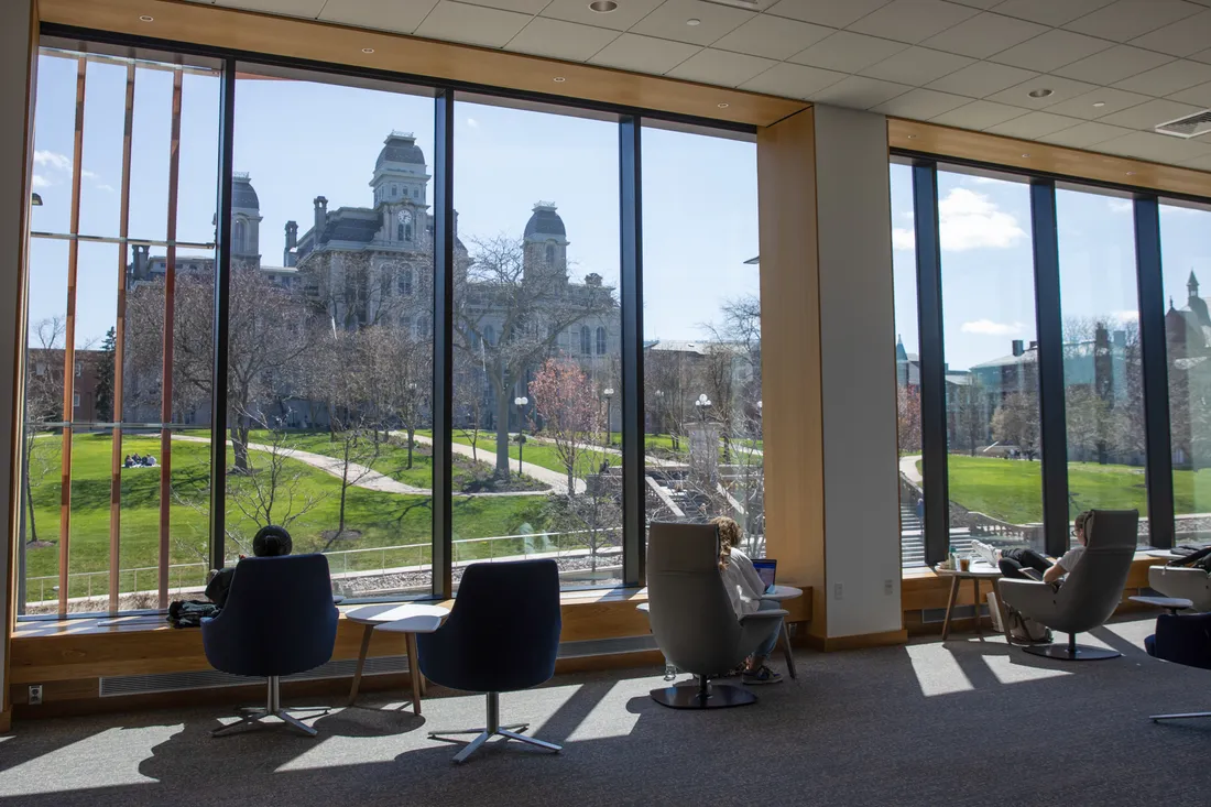 Student sitting on chairs in front of a large window with view of campus buildings.