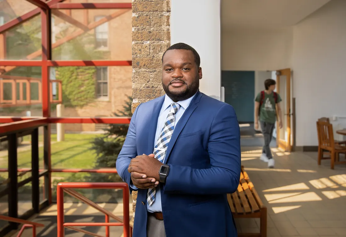 Terrance King posed in front of a window, smiling with his hands clasped in front of his body.