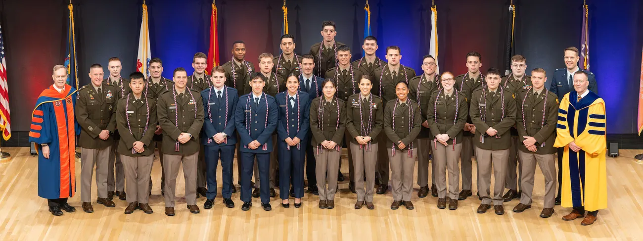 Army ROTC students and Air Force standing at attention wearing blue uniform at a celebration