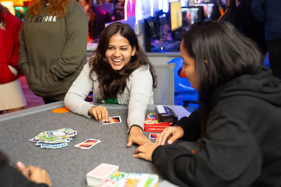 Student reaches across table playing card game at event.