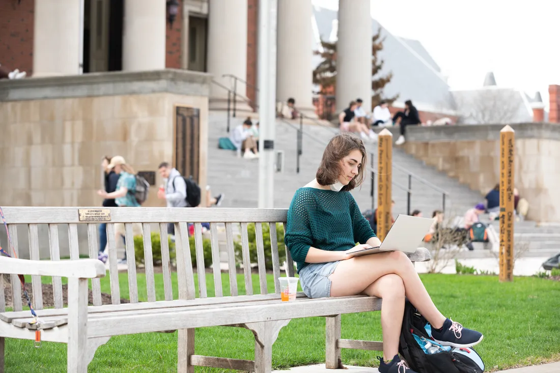 Student sitting on a bench outside on a college campus.