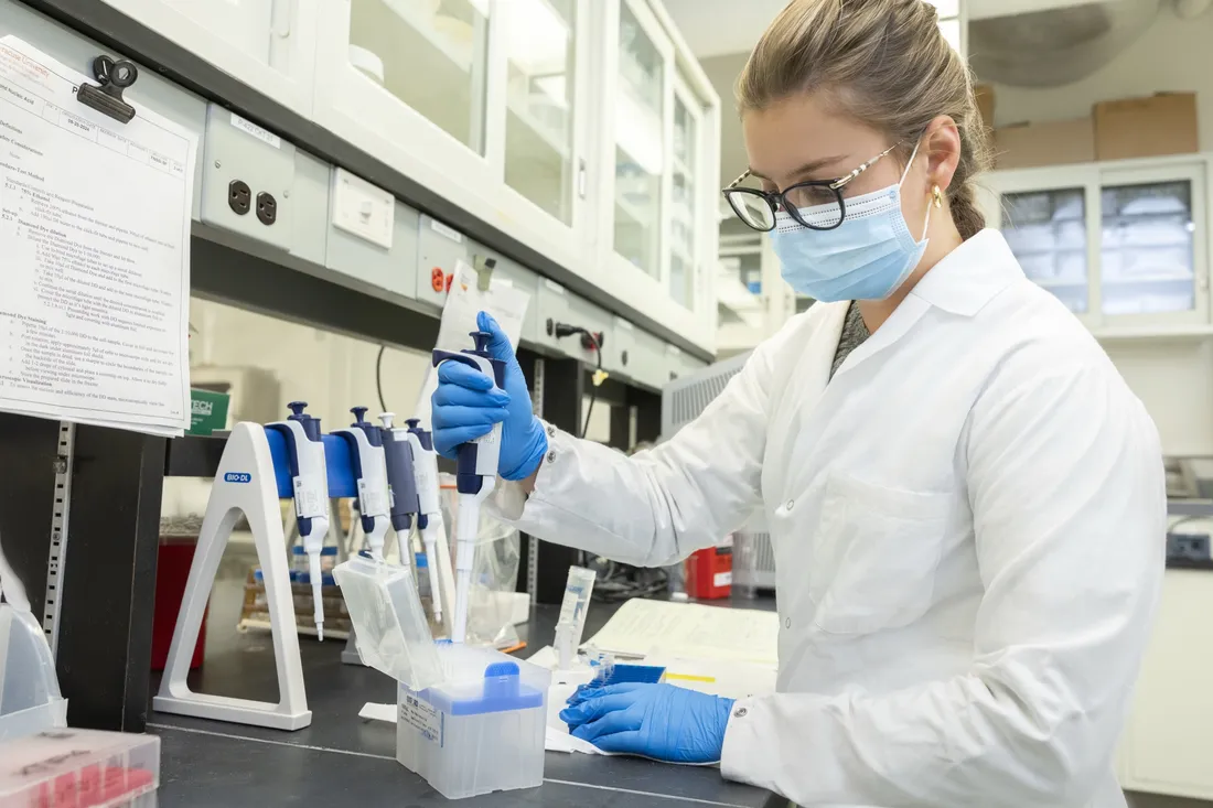 Person in a lab wearing lab coat and mask using a micropipette.
