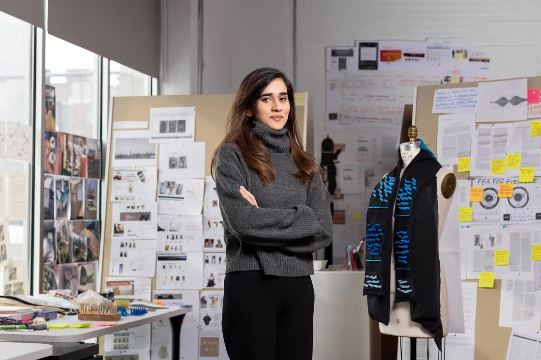 Photo of a female student standing next to a prototype of a scarf on a mannequin.